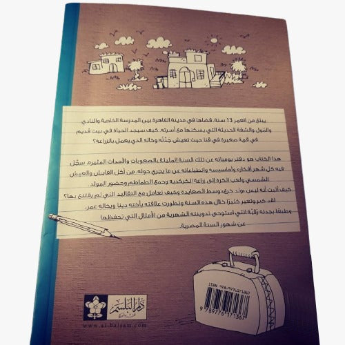 Book cover titled "سنة في قنا," an Arabic adventure story for children aged 9 to 12, featuring illustrations of a suitcase, buildings, and trees. The background resembles lined paper with Arabic text adorning the front and back.